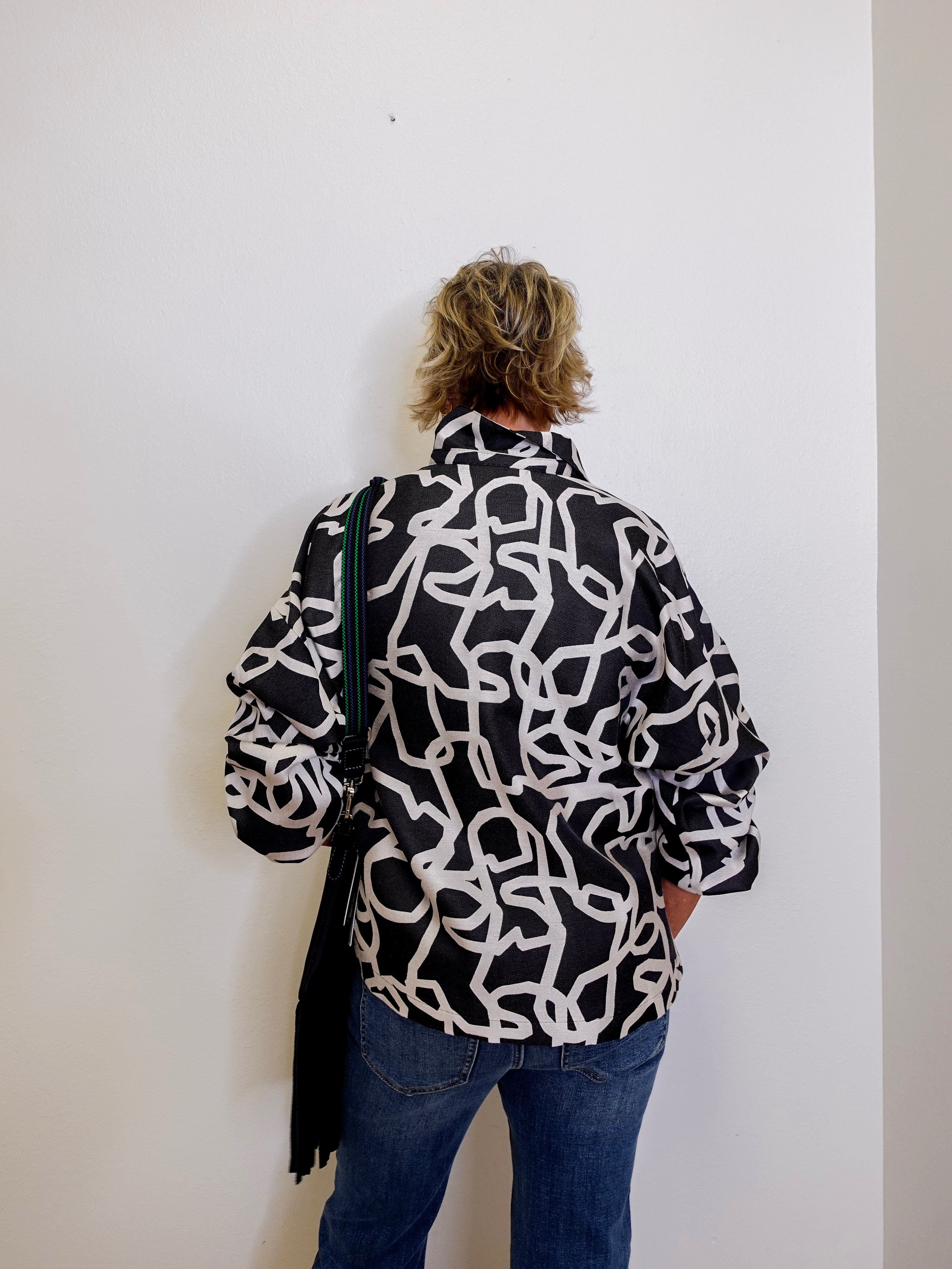 Person wearing a black and white patterned jacket against a white wall