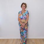 Woman in a floral dress holding a teddy bear against a white wall.