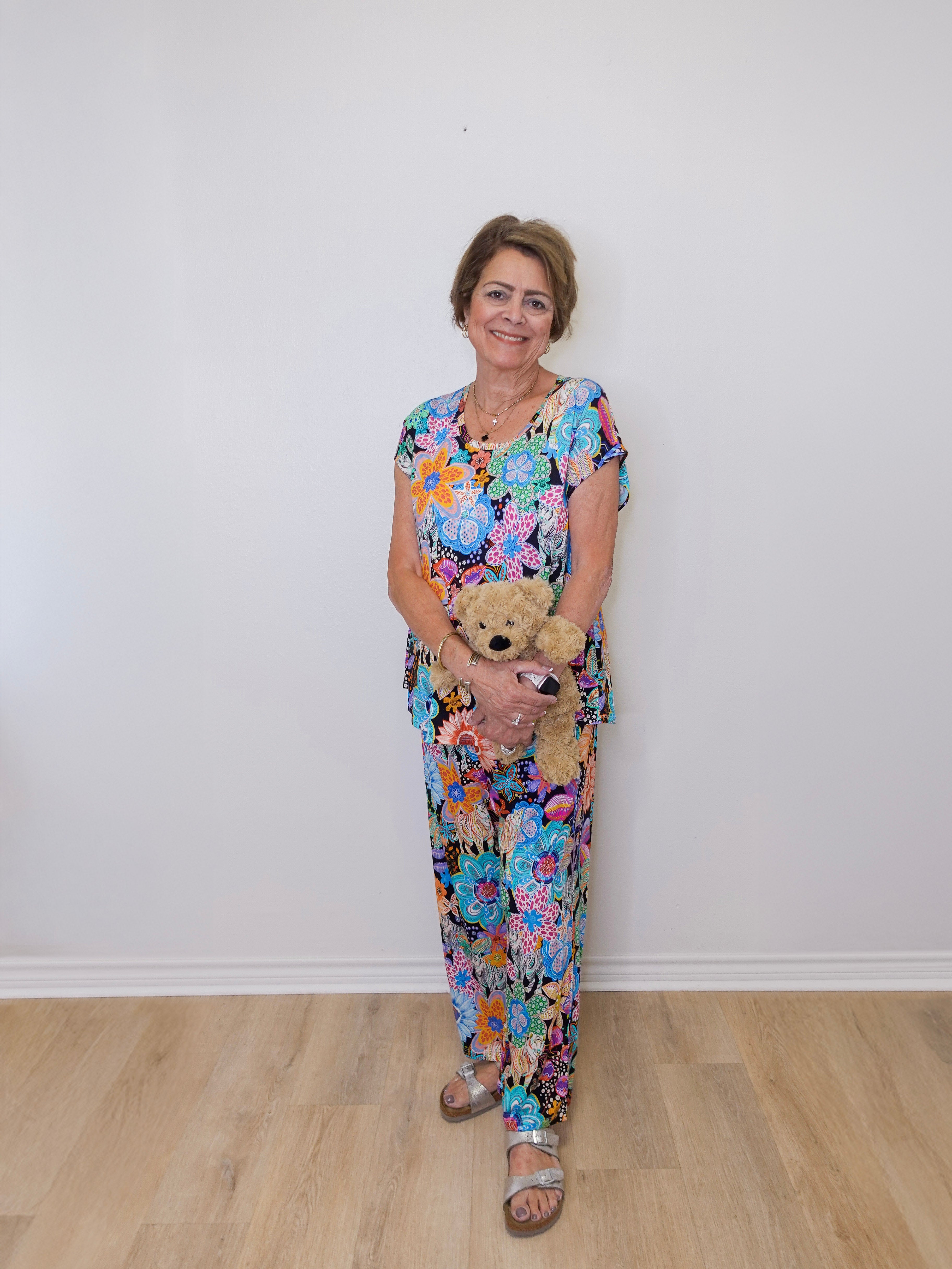 Woman in a floral dress holding a teddy bear against a white wall.