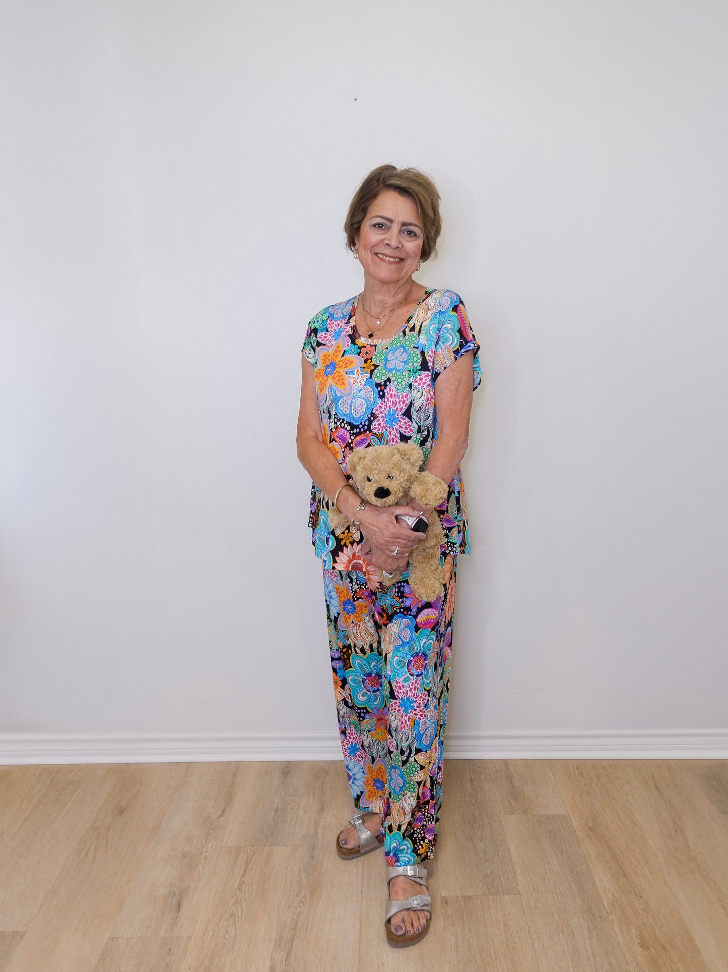Woman in a floral dress holding a teddy bear against a white wall.