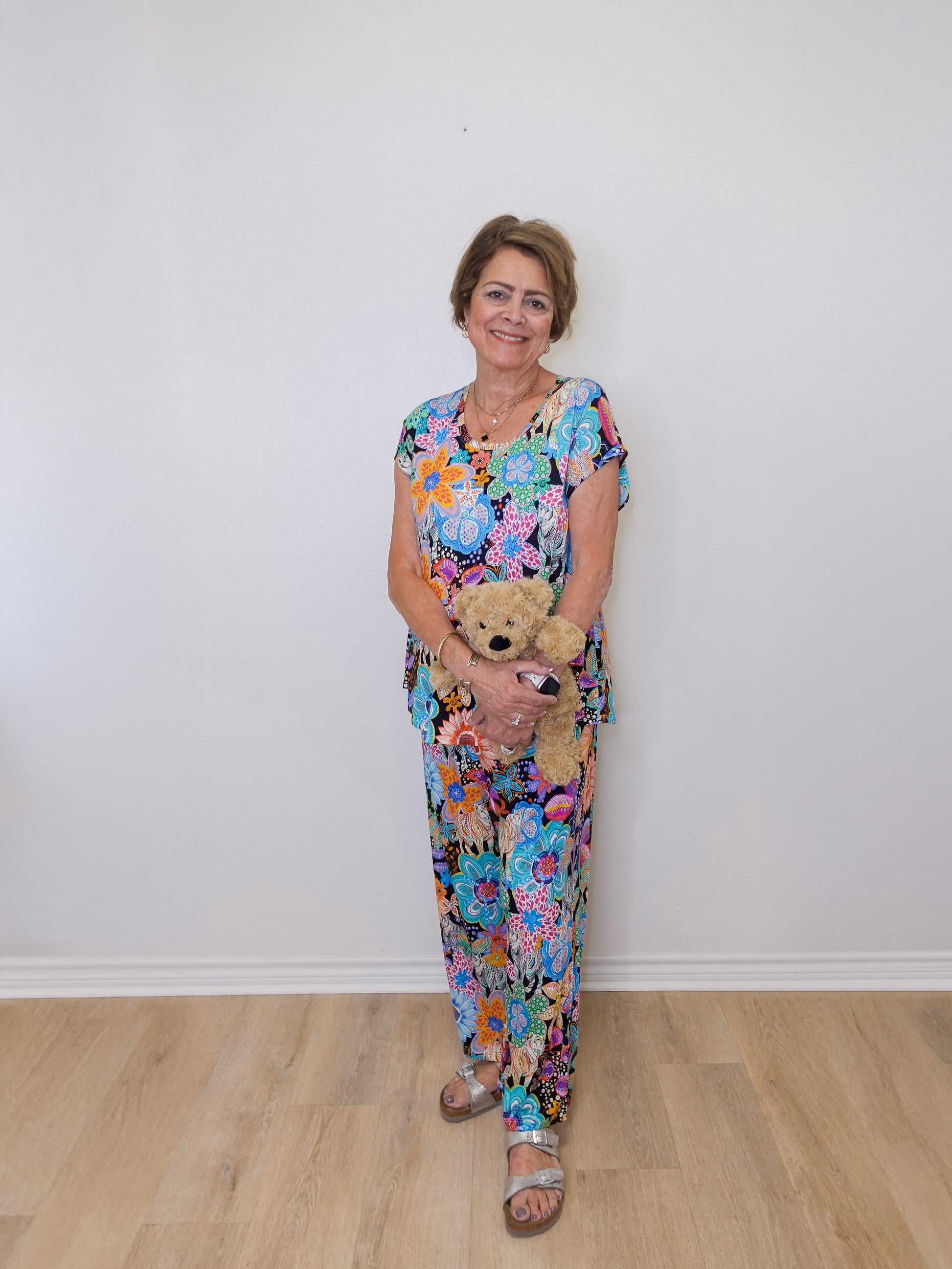 Woman in a floral dress holding a teddy bear against a white wall.