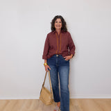 Woman wearing a plaid shirt and jeans, holding a beige handbag against a white wall.
