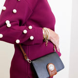 Person wearing a purple coat with pearl buttons holding a black handbag with brown accents.