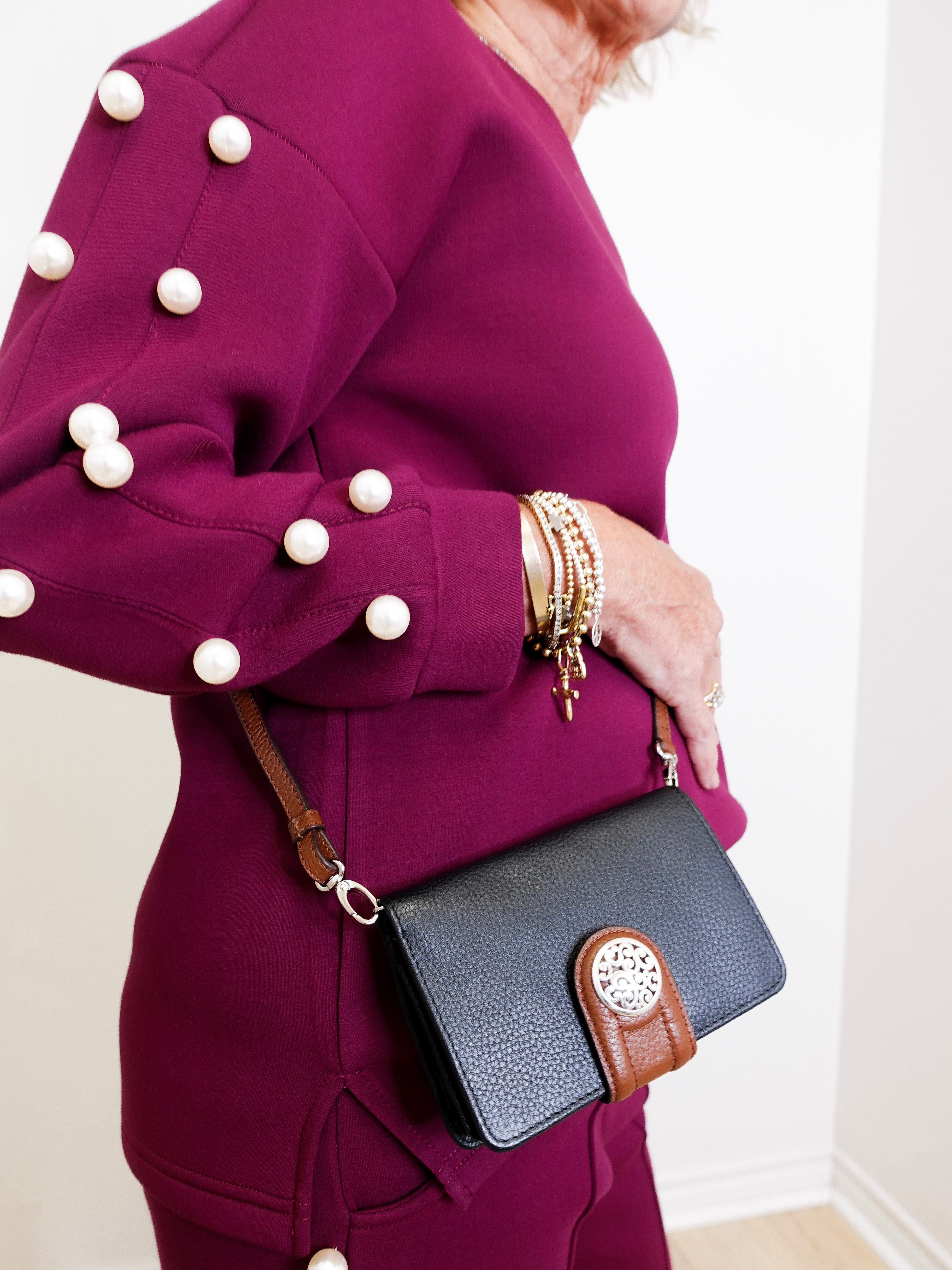 Person wearing a purple coat with pearl buttons holding a black handbag with brown accents.