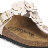 White sandal with floral designs and a gold buckle on a white background