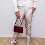 Person wearing a white sweater, beige pants, and white sneakers holding a red handbag against a white wall.