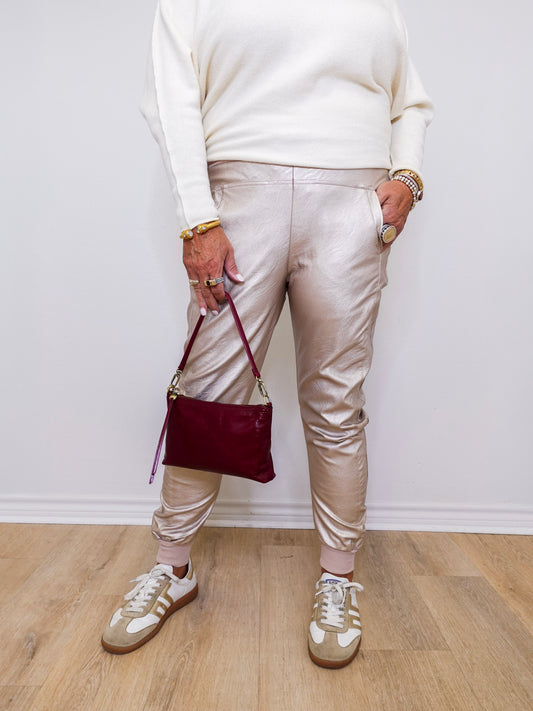 Person wearing a white sweater, beige pants, and white sneakers holding a red handbag against a white wall.