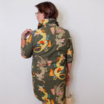 Woman wearing a green dress with dragon pattern against a white wall
