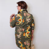 Woman wearing a green dress with dragon pattern against a white wall