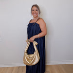 Woman in a navy dress holding a gold handbag against a white wall.