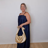 Woman in a navy dress holding a gold handbag against a white wall.