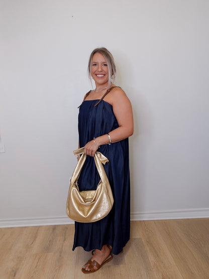 Woman in a navy dress holding a gold handbag against a white wall.