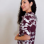 Woman wearing a maroon and white patterned blouse against a plain background