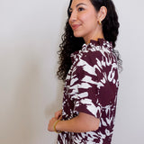Woman wearing a maroon and white patterned blouse against a plain background