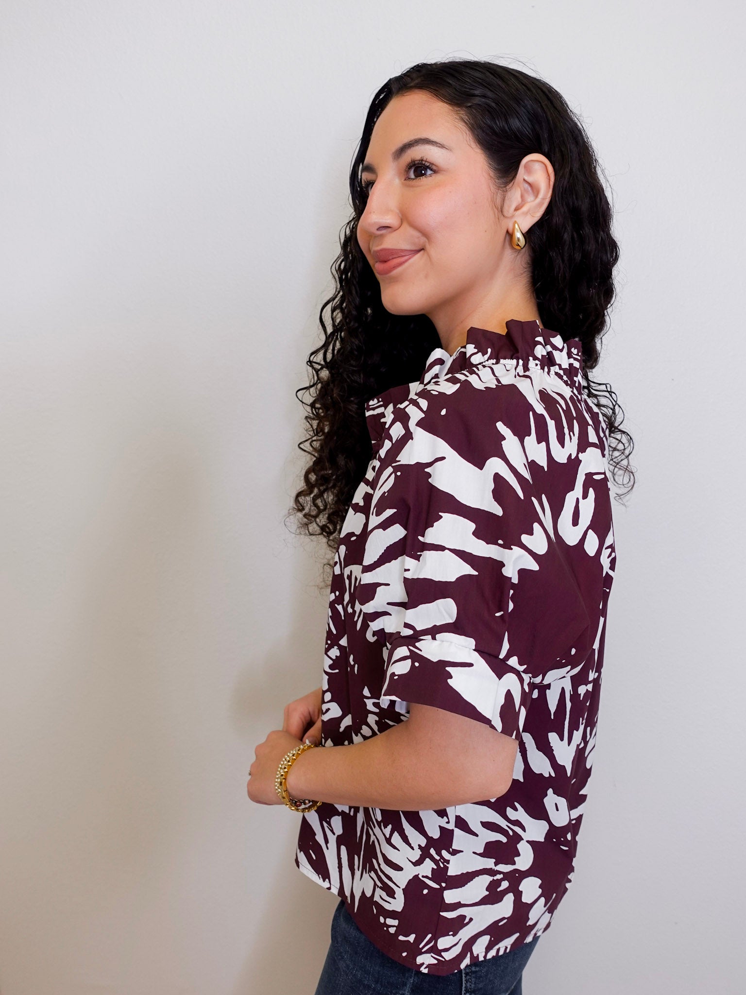 Woman wearing a maroon and white patterned blouse against a plain background