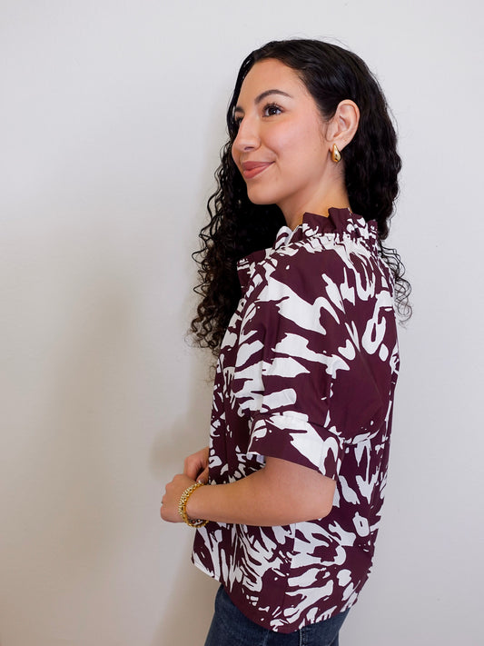 Woman wearing a maroon and white patterned blouse against a plain background