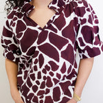 Person wearing a maroon and white patterned blouse against a plain background