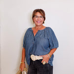Woman wearing a blue blouse and black pants against a white wall