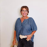 Woman wearing a blue blouse and black pants against a white wall