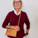 Woman wearing a maroon sweater and holding a tan handbag against a plain background