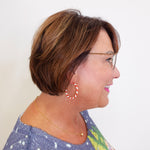 Woman with short brown hair wearing glasses and hoop earrings against a white background