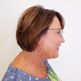 Woman with short brown hair wearing glasses and hoop earrings against a white background