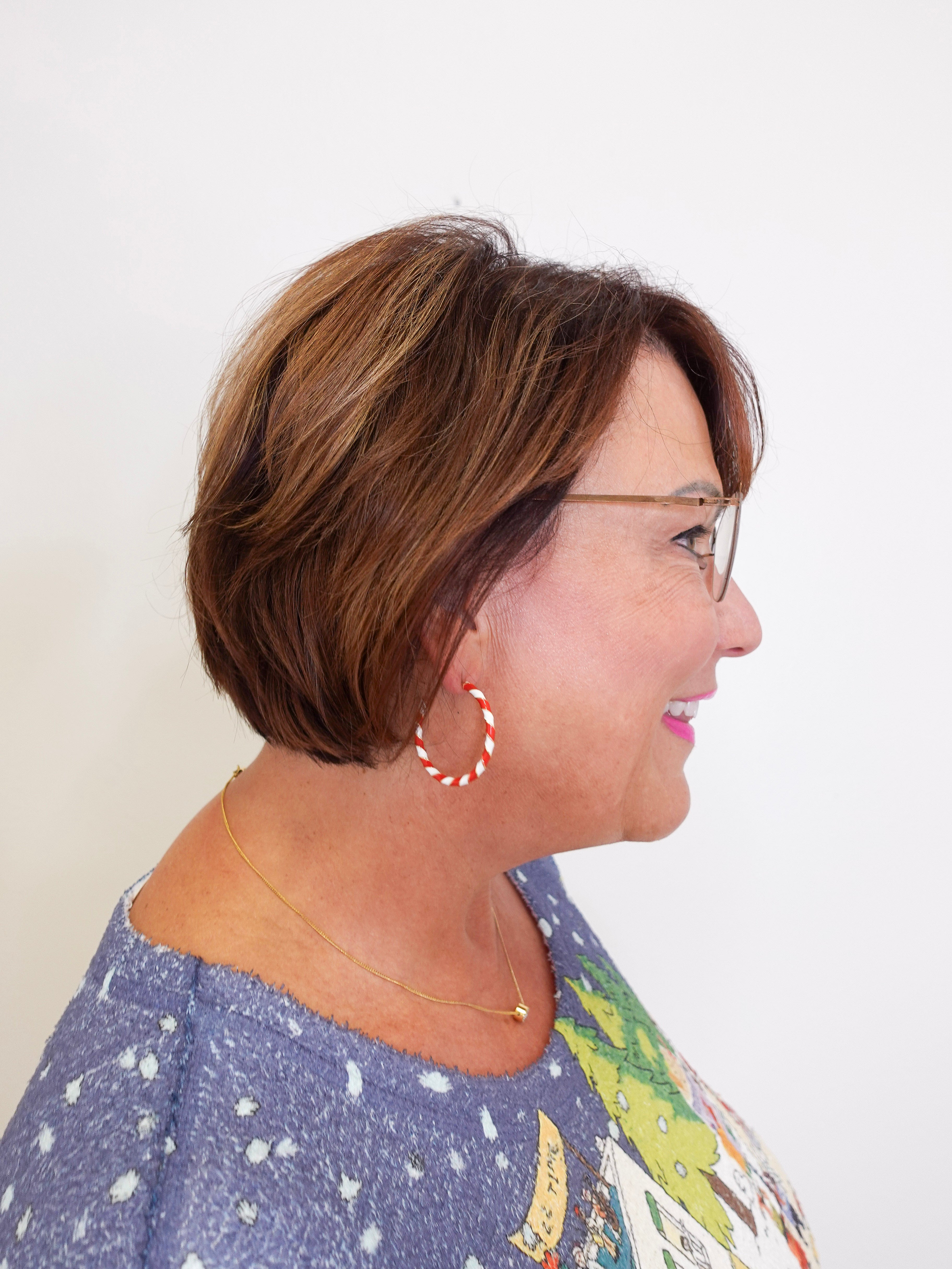 Woman with short brown hair wearing glasses and hoop earrings against a white background