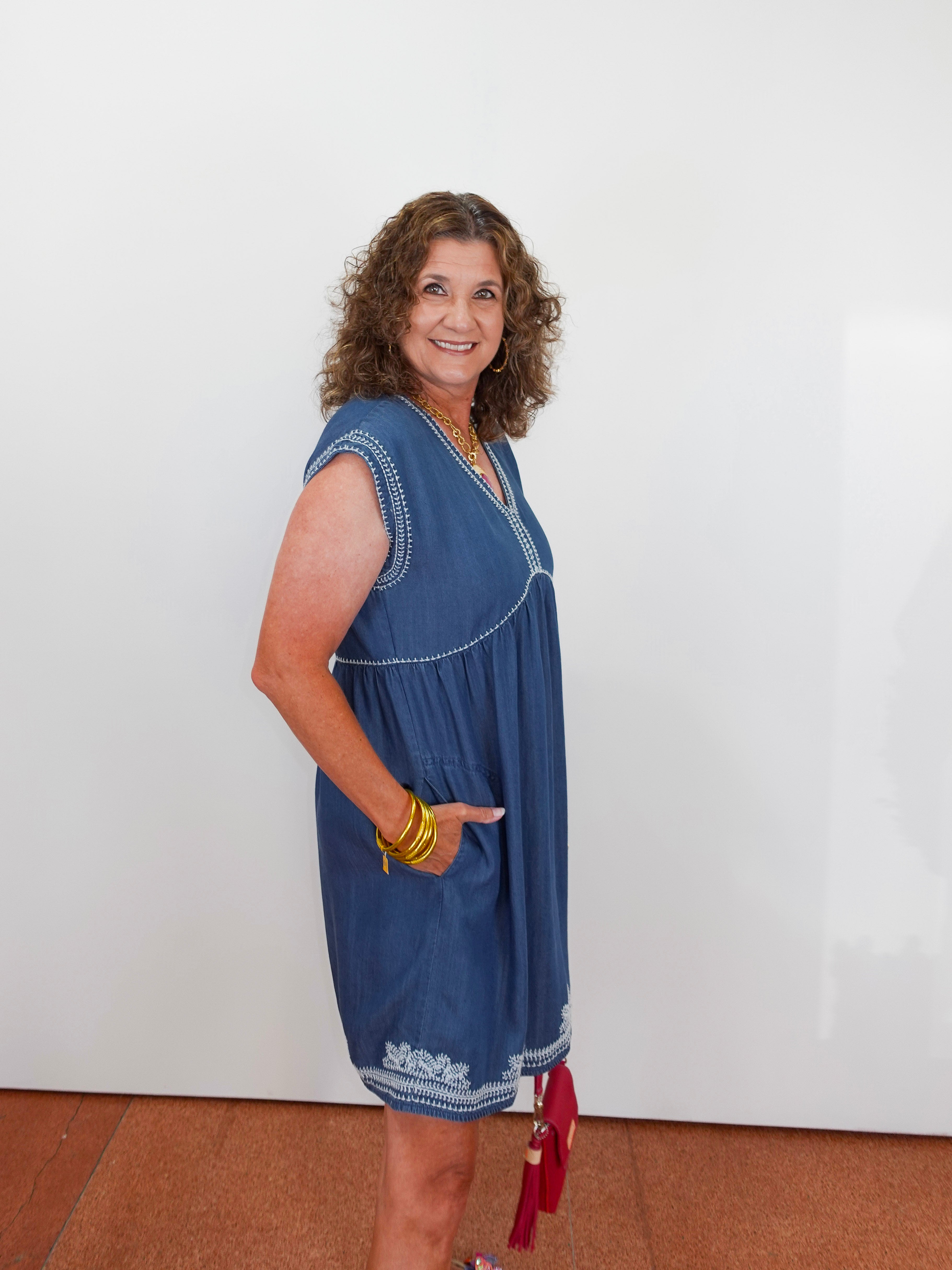 Woman wearing a blue dress with white embroidery against a white wall.