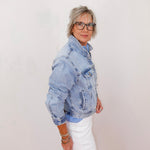 Person wearing a denim jacket and white pants against a plain background