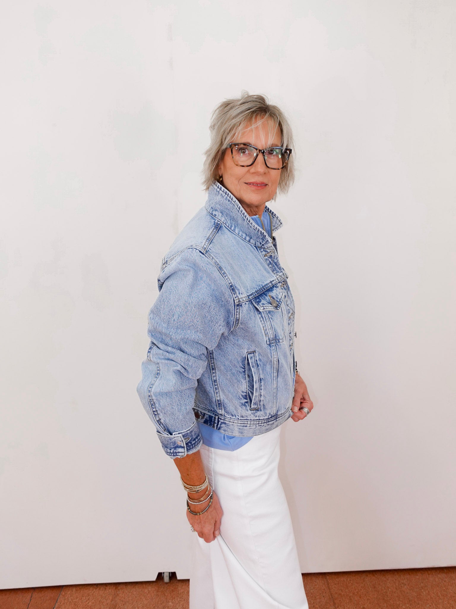 Person wearing a denim jacket and white pants against a plain background
