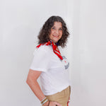 Woman wearing a white shirt with text and a red scarf, standing against a plain background