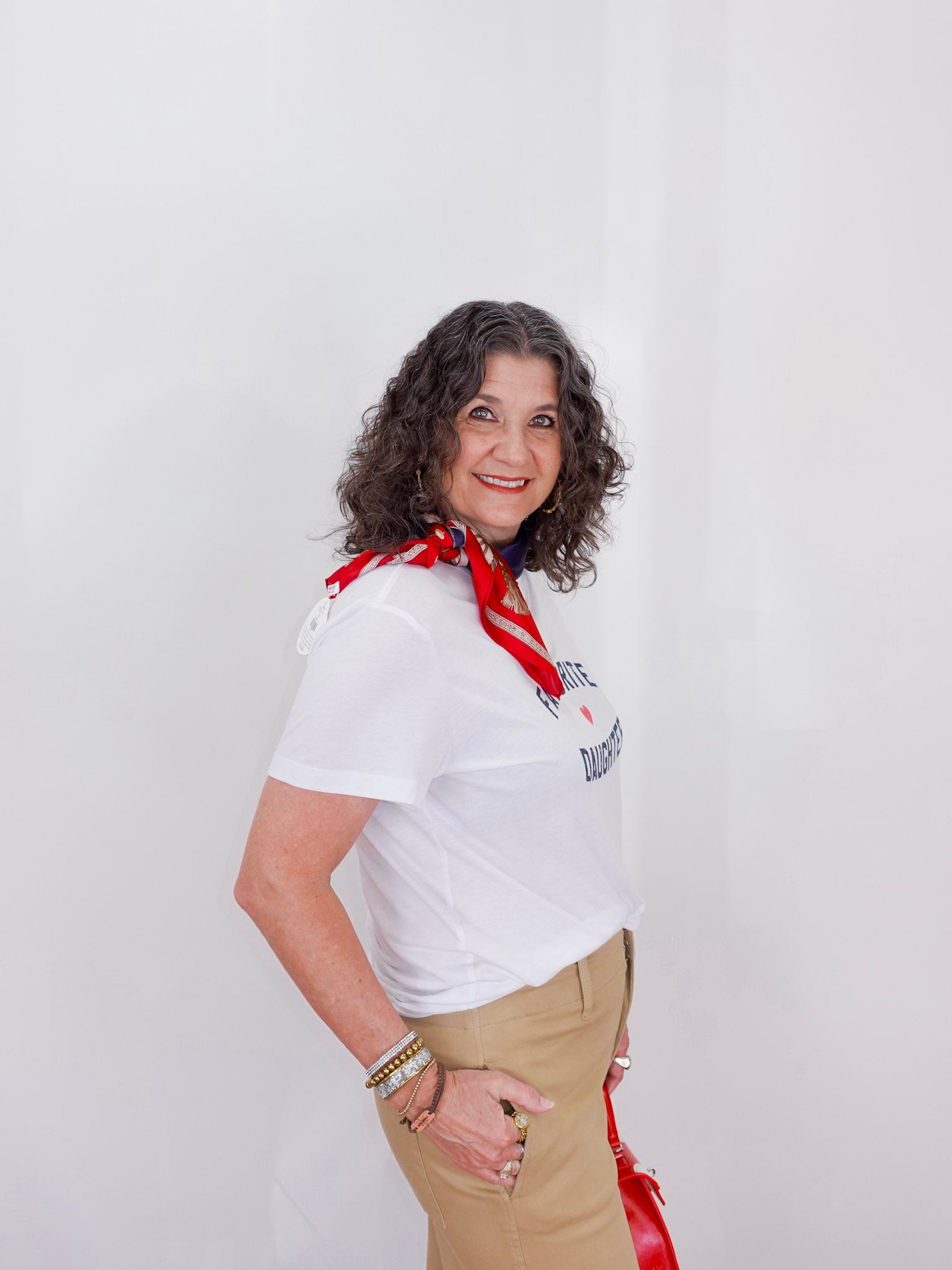 Woman wearing a white shirt with text and a red scarf, standing against a plain background