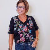 Woman wearing a black top with colorful floral embroidery against a white background