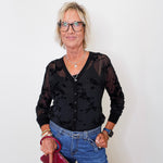 A woman modeling a 2 piece mesh cardigan tank set in black with blue jeans, while holding a maroon purse against a white wall.