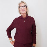 Person wearing a maroon sweater and pants against a white wall