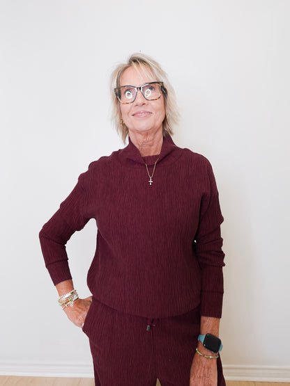 Person wearing a maroon sweater and pants against a white wall