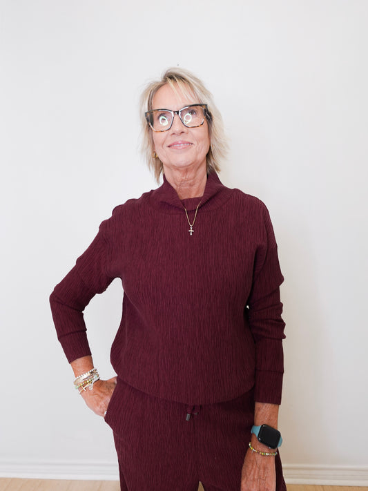 Person wearing a maroon sweater and pants against a white wall