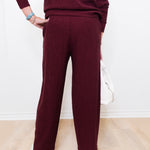 Person wearing a burgundy sweater and pants on a light wooden floor.