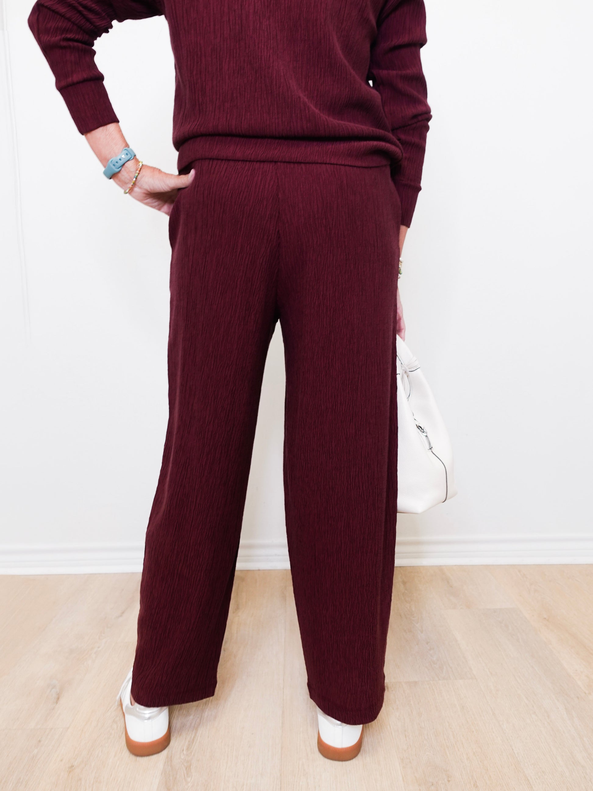 Person wearing a burgundy sweater and pants on a light wooden floor.