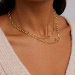 Gold chain necklace with a heart pendant on a person wearing a beige sweater.