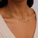 Gold chain necklace with a heart pendant on a person wearing a beige sweater.