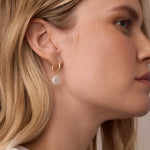 Close-up of a woman wearing gold hoop earrings with a neutral background