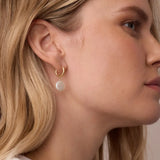 Close-up of a woman wearing gold hoop earrings with a neutral background