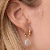 Gold hoop earring with a pearl drop worn by a person with blonde hair.