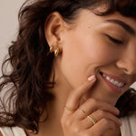 Woman wearing gold hoop earrings and rings with a neutral background