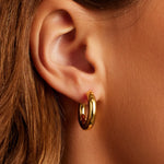 Close-up of an ear wearing a gold hoop earring with a blurred background
