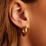 Close-up of an ear wearing a gold hoop earring with a blurred background