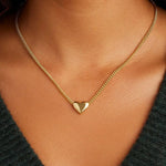 Gold heart necklace on a person wearing a dark green top