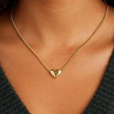 Gold heart necklace on a person wearing a dark green top