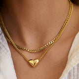 Gold chain necklace with a heart pendant on a person wearing a white top.